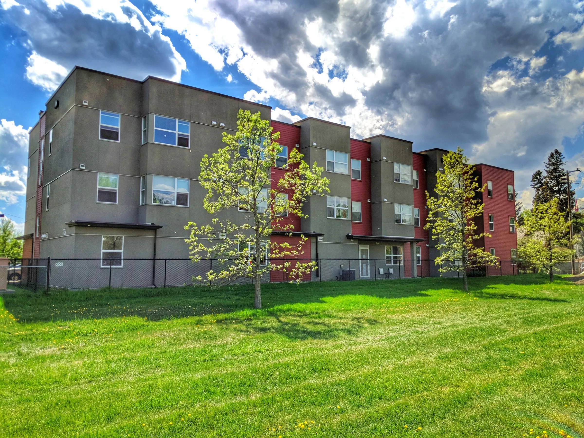 Inglewood House, a three-storey red and grey apartment building, behind a green lawn and young trees on a sunny day