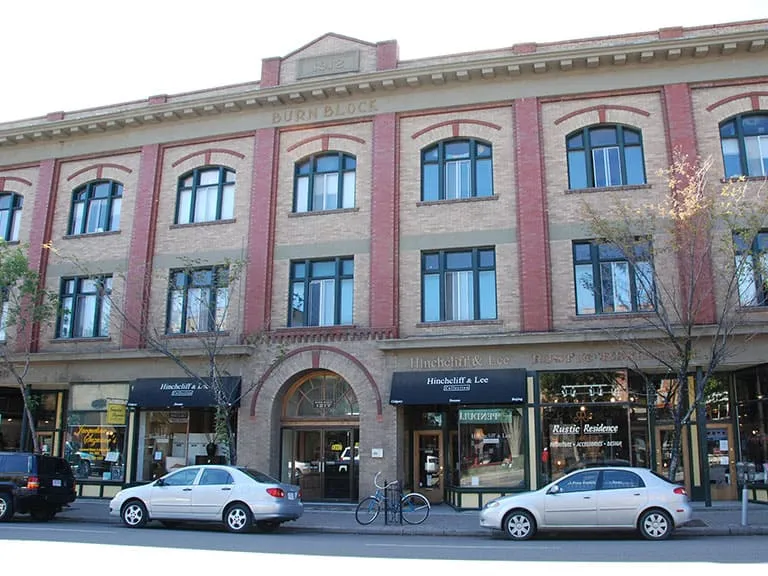 A long three-storey heritage building with arched windows and shops along 9th Avenue