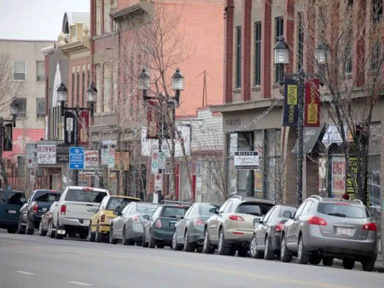 Cars parked along a tree-lined stretch of 9th Avenue with historic storefronts and lamp posts